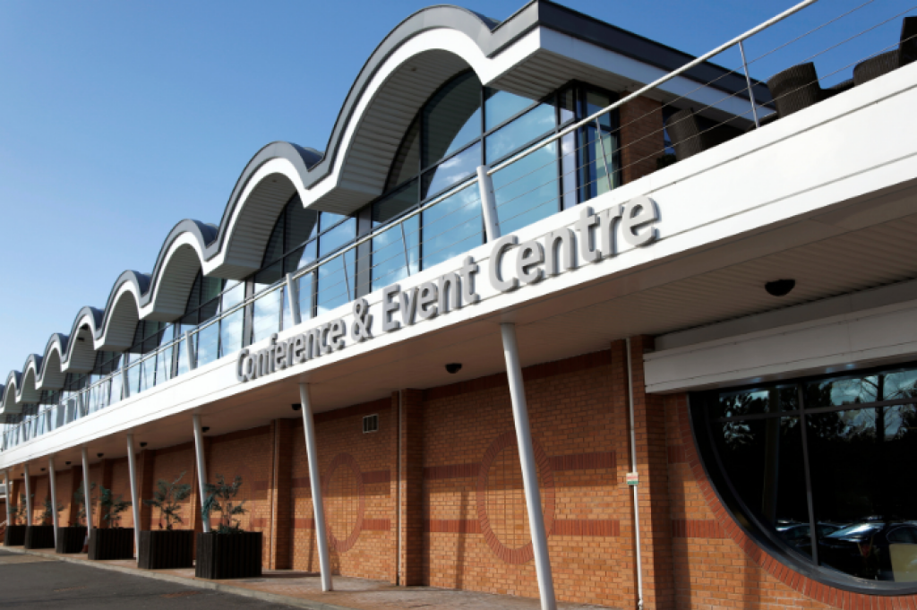 Cranmore Park conference and exhibition centre in Solihull West Midlands is the home of INDX Shows. An image of the frontage of Cranmore Park features central. The curved architraves highlighted by the clear blue sky behind.