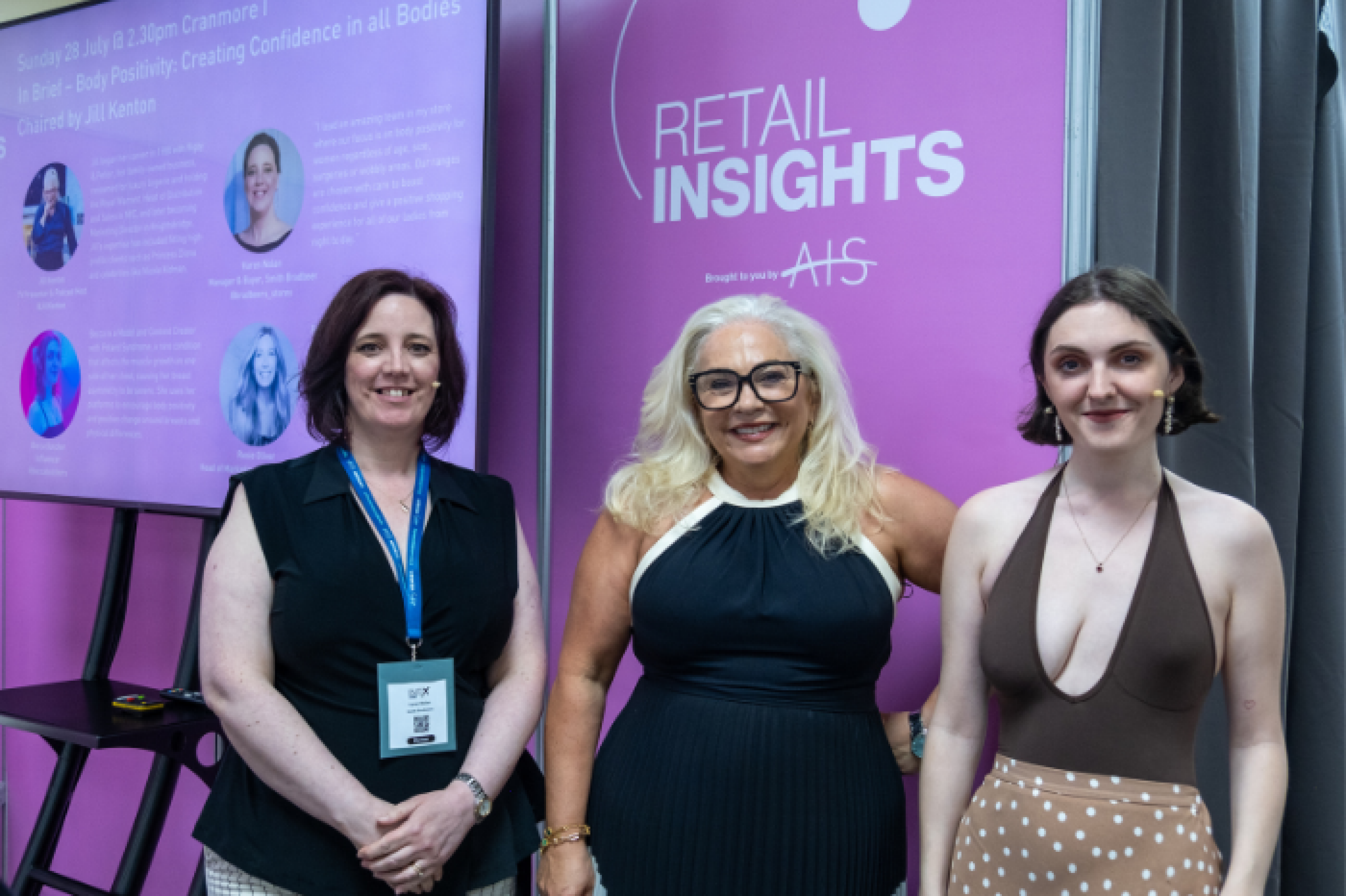 Photo of three women wearing microphones and smiling for the camera at Retail Insights - an industry talk at the INDX Intimate Apparel lingerie trade show at Cranmore Park. In the background there is a purple screen and branded background featuring the AIS logo, Retail Insights, and Key Speakers.